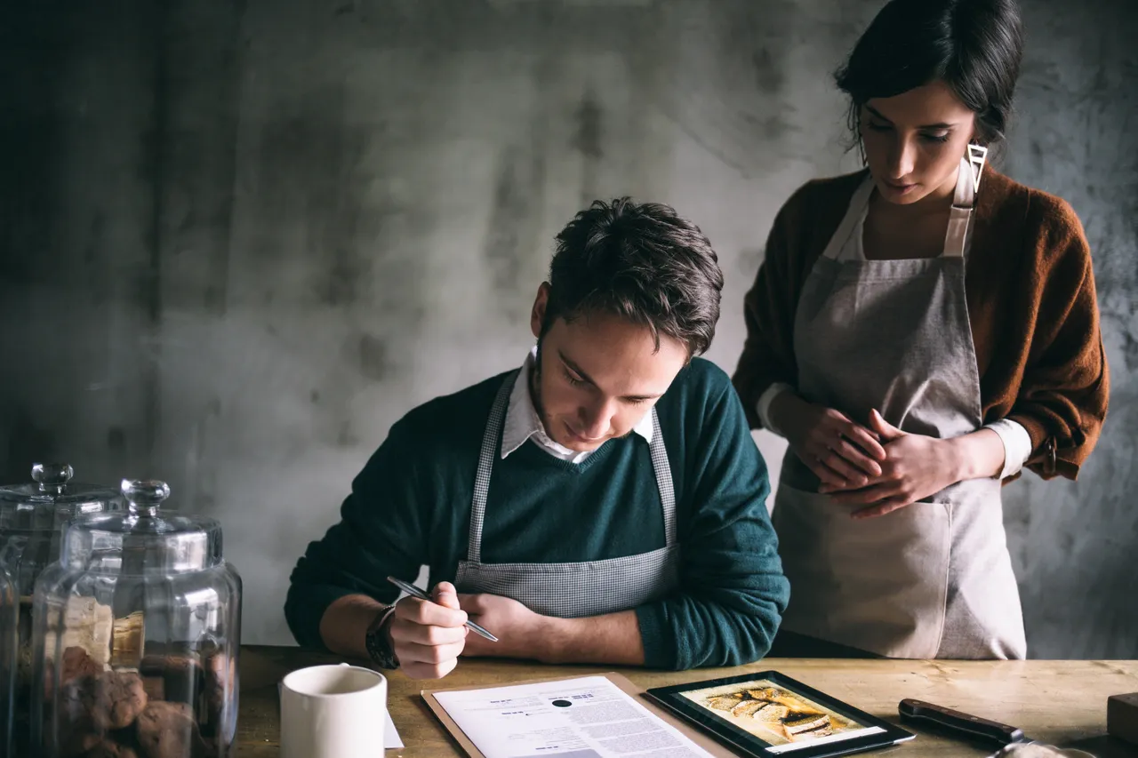 A couple sit at a table reviewing a cooking recipe