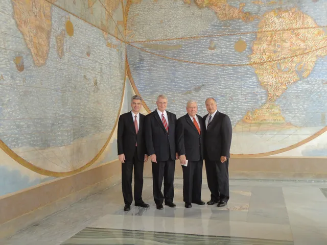 President Gérald Caussé, Bishop Richard C. Edgley, Elder M. Russell Ballard, and Elder Ronald A. Rasband stand in front of a large world map at the Vatican.