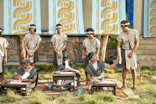 Scribes sit, taking notes on parchment of what King Benjamin is teaching in the Land of Zarahemla. Behind them, runners stand ready to take the teachings to the Nephite people.