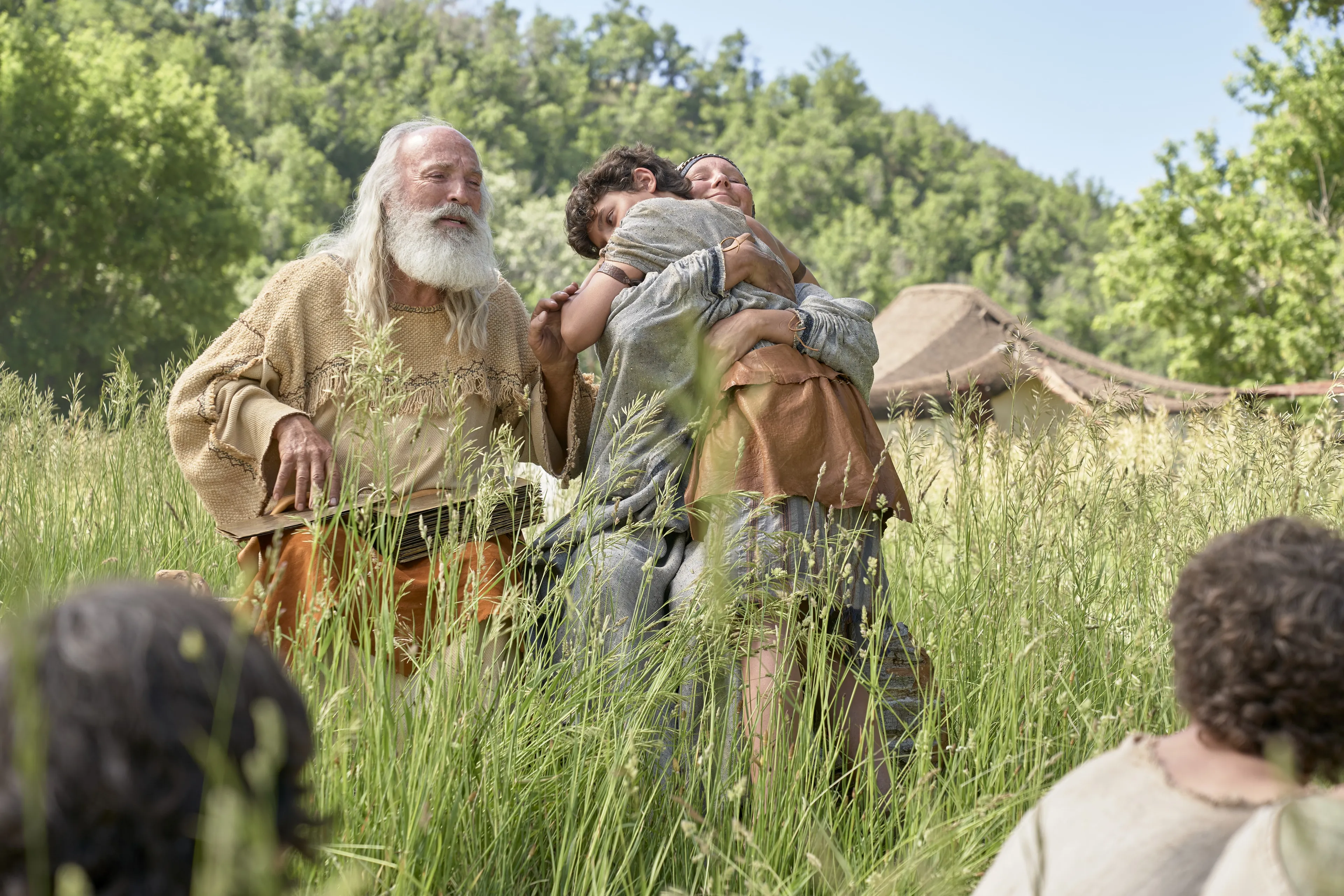 Sariah hugs Joseph as Lehi teaches their family from the plates of brass.