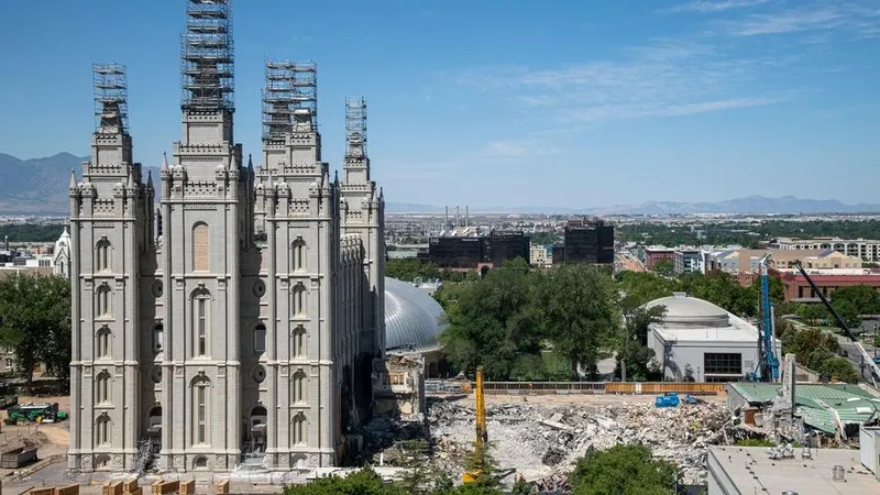 The Salt Lake Temple is under construction. The grounds are torn up and large trucks are in the midst of the debris. This is an overview shot of the grounds and temple.  