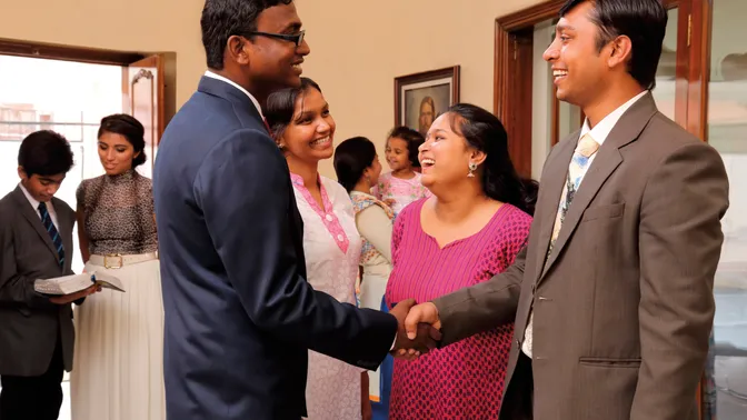 Members are shaking hands and greeting each other in a foyer of a meetinghouse in India.