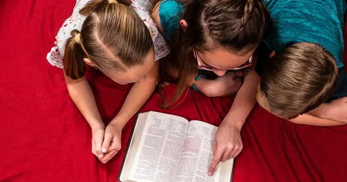 Primary children read the Book of Mormon in Spanish while huddled together on the floor.