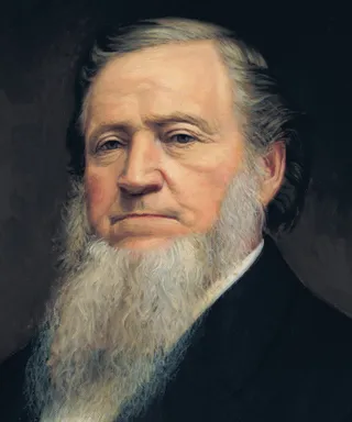Formal head and shoulders portrait of Brigham Young. He is depicted in his seventies wearing a wearing a dark suit and vest, (painted probably by photograph and aided by Clawson's memory) with a long beard.