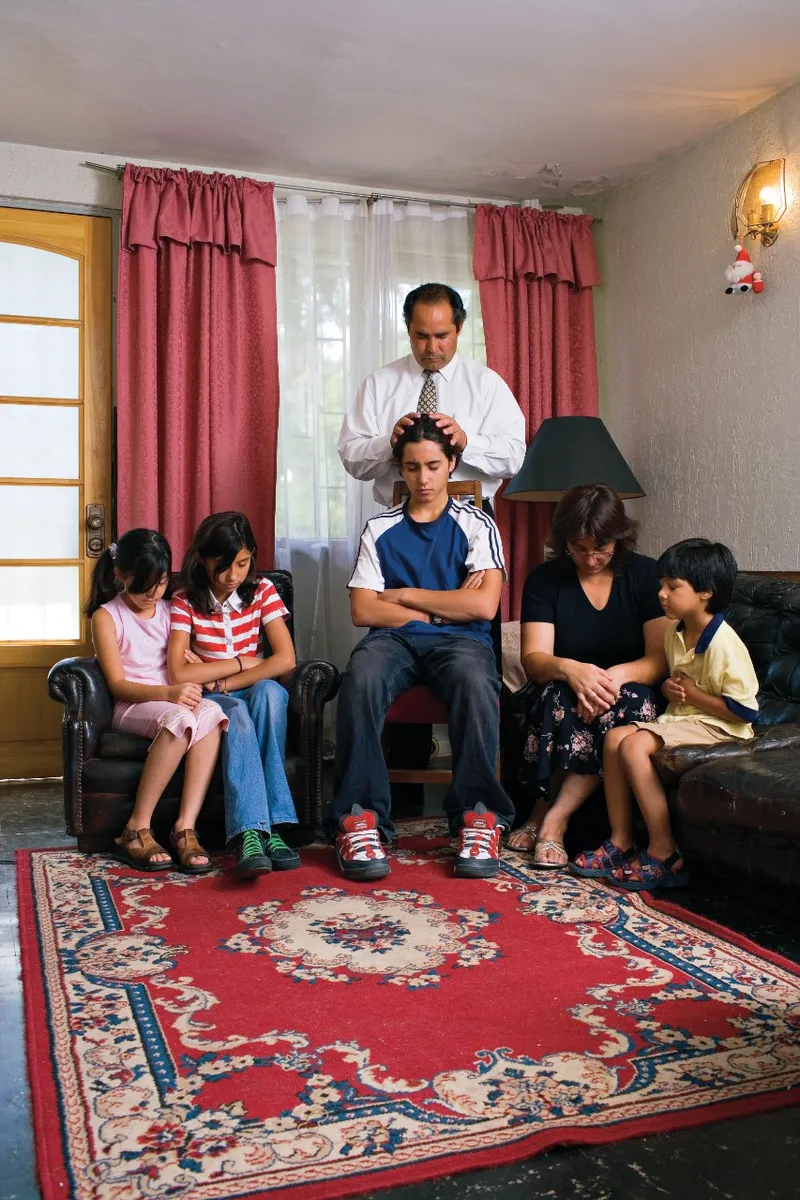 A father gives a blessing to his son while the other family members listen.