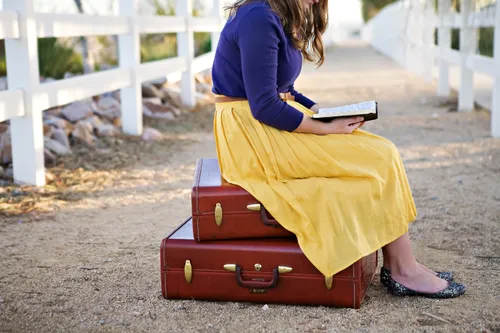 girl sitting on a suitcase reading the scriptures