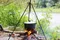 A pot is hanging over a campfire. Dinner is being cooked over an open flame. There is a river or lake in the background.