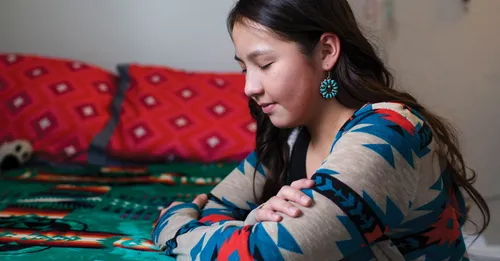A young woman praying while kneeling at her bedside.
