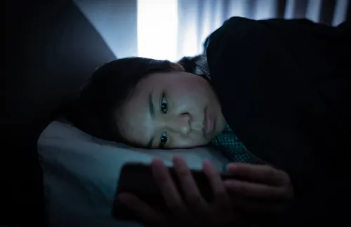 a woman lying in bed and staring at a phone