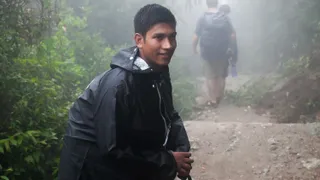 A young man walking with a walking stick on a trail.