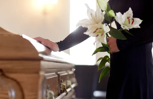 a mourner holding flowers and standing next to a coffin