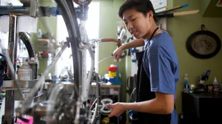 A young Asian man working on a bicycle.