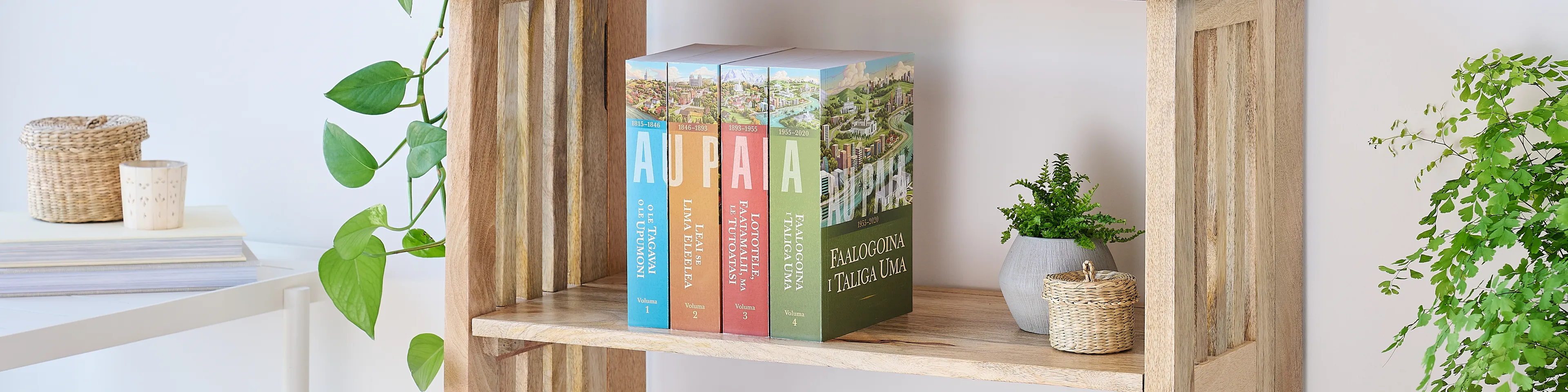 Picture of the book series, 'Saints' volume 1-4 (Samoan edition). Four volumes are arranged on the middle shelf of a wooden bookshelf along with plants.