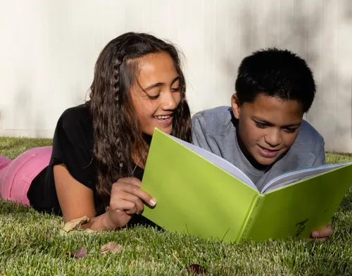 Girl and. boy reading a book together on the grass on a sunny day