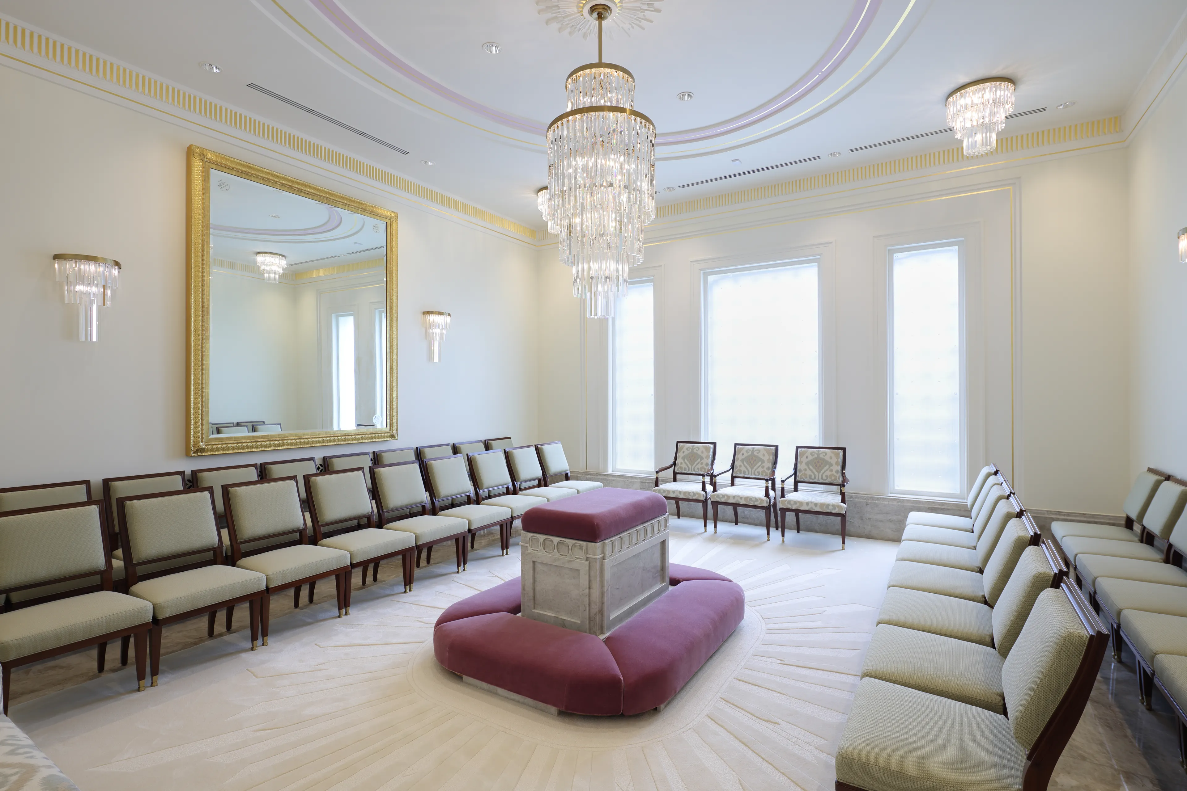 Interior image of the Abidjan Ivory Coast Temple featuring a Sealing Room. There is an altar in the middle of the room with a chandelier suspended above. There are chairs to three sides and a large window on the far side wall © undefined ipCode 1.