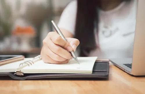 a woman’s hand holding a pen over a notebook