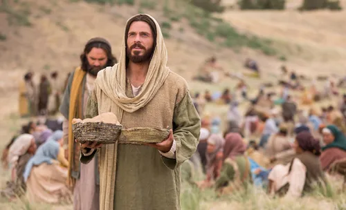 Jesus Christ holding baskets of bread and fish, with many people behind him