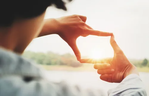 hands framing the sun as it sets