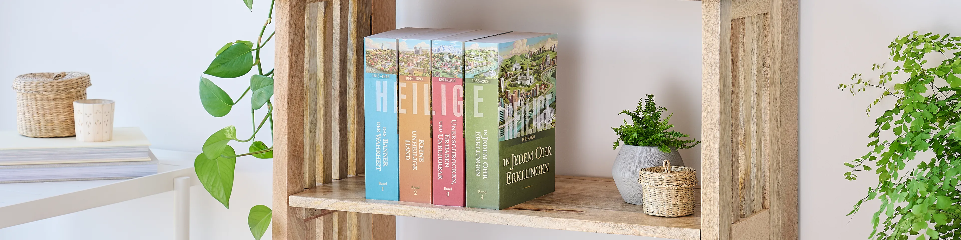 Picture of the book series, 'Saints' volume 1-4 (German edition). Four volumes are arranged on the middle shelf of a wooden bookshelf along with plants.