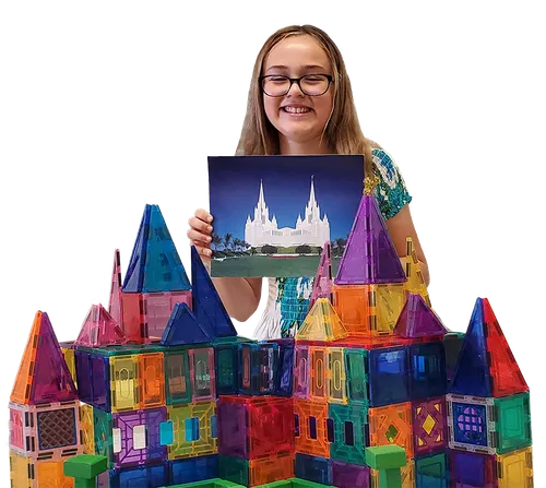 A girl holding a picture of a temple and sitting with a temple made from magnet blocks