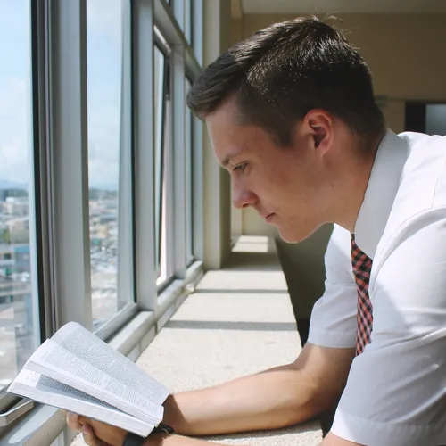 a young adult reading the scriptures next to a window