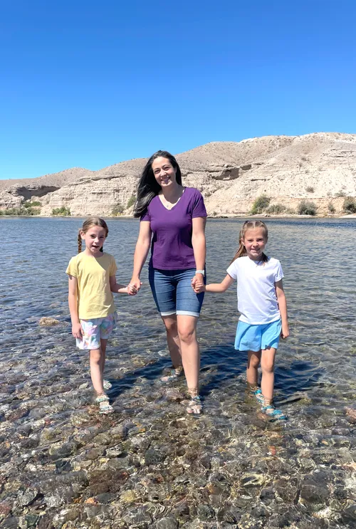 Girls walking in the river while holding hands with their mom
