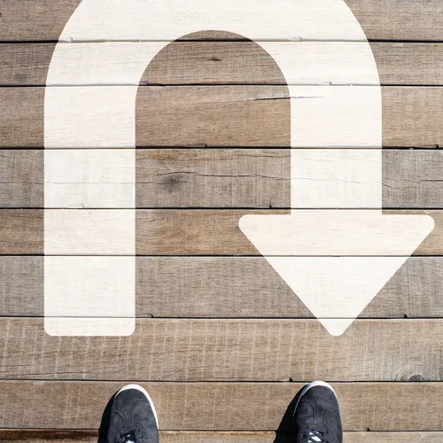 a pair of feet standing in front of a U-turn symbol painted on a wooden path