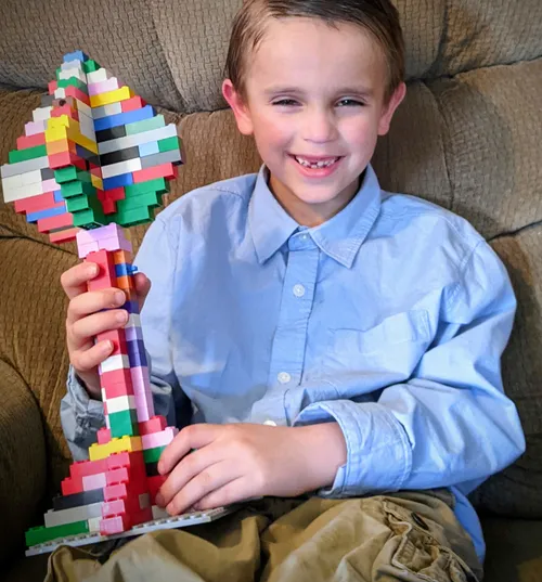 Boy holding plastic brick creation in the shape of a tree