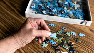 Man's hand holding corner piece of blue jigsaw puzzle.  (horiz)