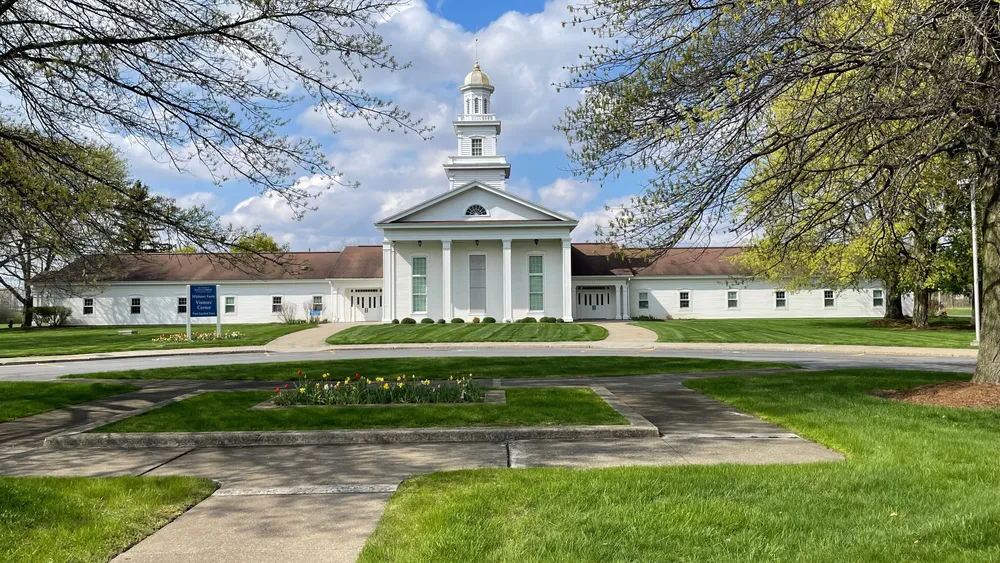 Large white meetinghouse with sign reading “Whitmer Farm Visitors’ Center”