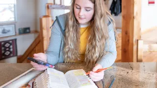 Girl studying and marking scriptures with help from a smartphone and lesson manual.