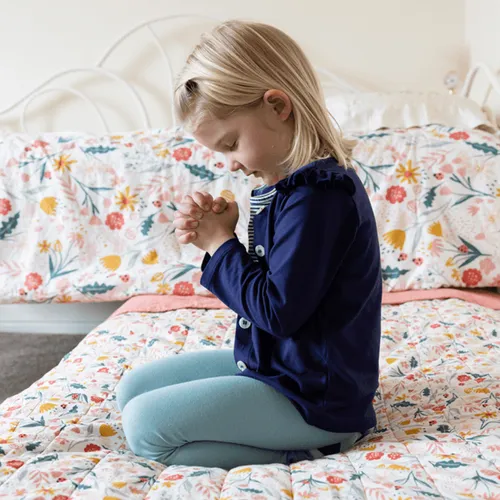 A girl kneeling on a bed to pray