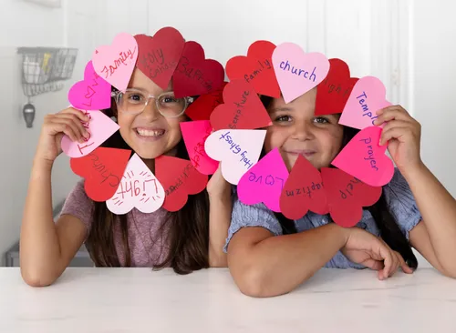 Two girls holding up paper heart wreaths