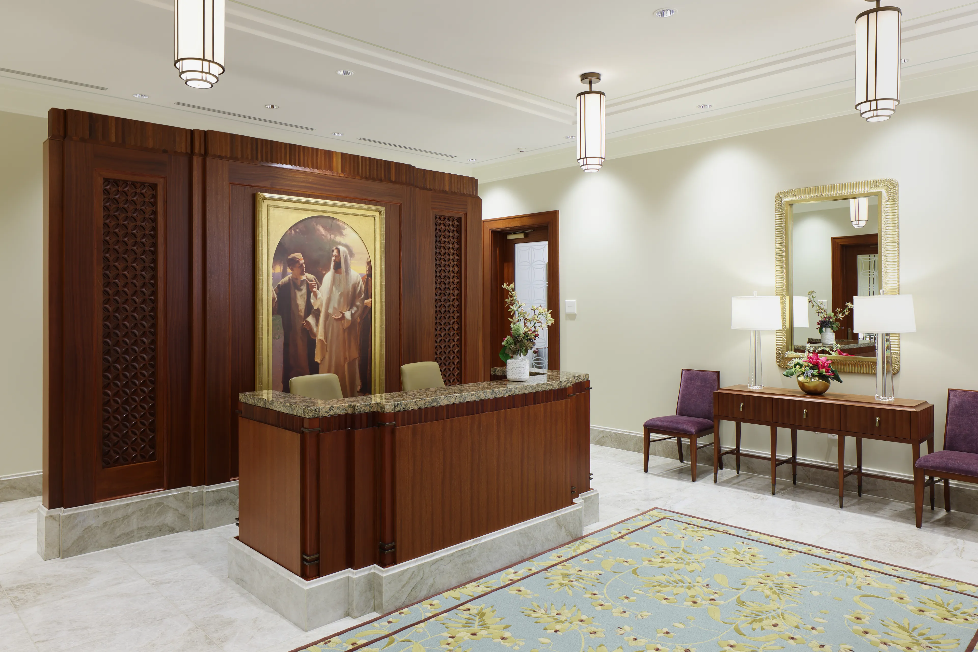 Interior image of the Abidjan Ivory Coast Temple featuring the Recommend desk. We see the desk with art of the Savior behind it. There are two chairs and a sidetable on one wall. © undefined ipCode 1.